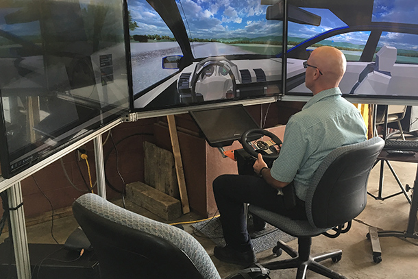 Man sitting in front of three TV screens driving an augmented reality vehicle.
