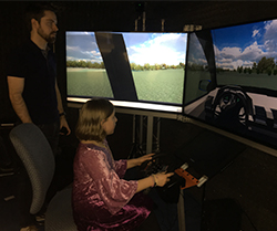 male graduate student watches female second grader drive a virtual reality simulator.