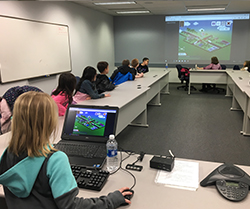 female student sitting in conference room playing a computer game that is projected onto a screen