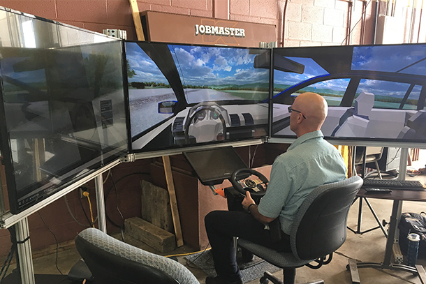man sitting in front of three TV screens driving an automated driving simulator